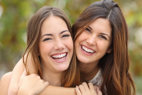 Two women friends laughing with a perfect white teeth with a green background